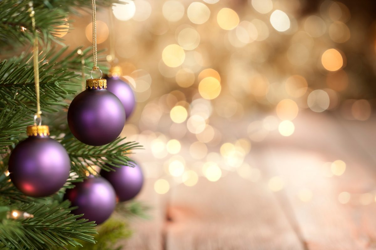 Christmas tree with purple baubles and gold lights against an old wood background